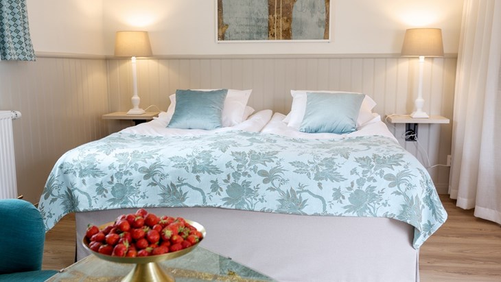 En dubbelsäng med ljusblått överkast och ett sängbord som det står jordgubbar på.