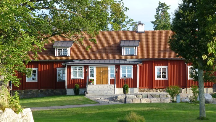 Ett rött, stort hus med mörkgul dörr och vita fönster.
