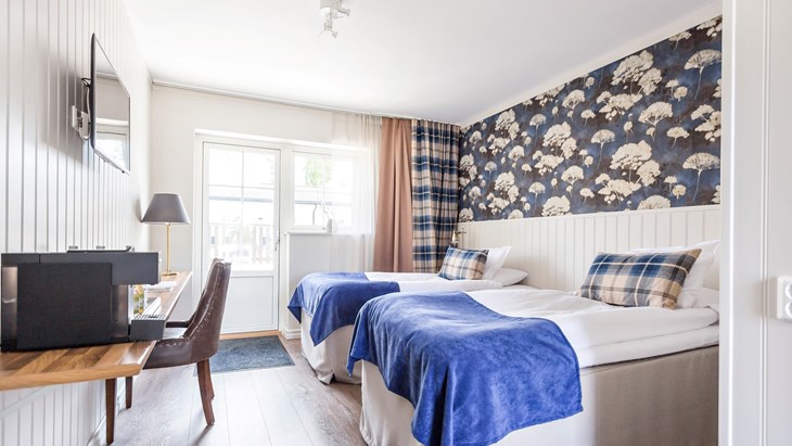 Ett av Katrinelunds gästgiveris rum med säng, skrivbord, stol och TV inrett i vitt och blått.