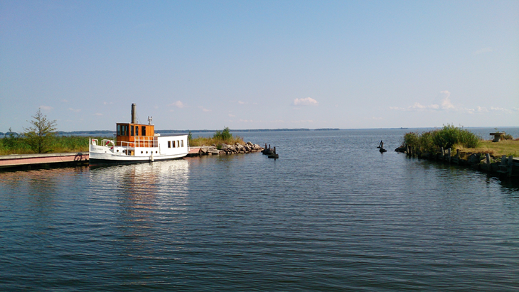 En vit ångbåt med trädetaljer i äldre stil ligger förtöjd vid en hamn.