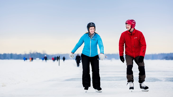 Två personer med hjälm åker skridskor på isen.