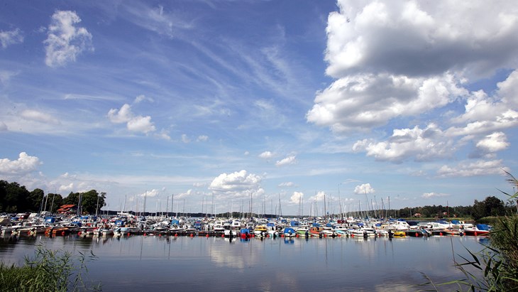 Sommarbild över sundbyholms gästhamn. Stort antal båtar som ligger förtöjda vid en brygga i Mälaren. 